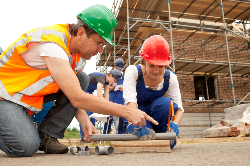 man with hard hat on construction site showing a woman with hard hat how to do something